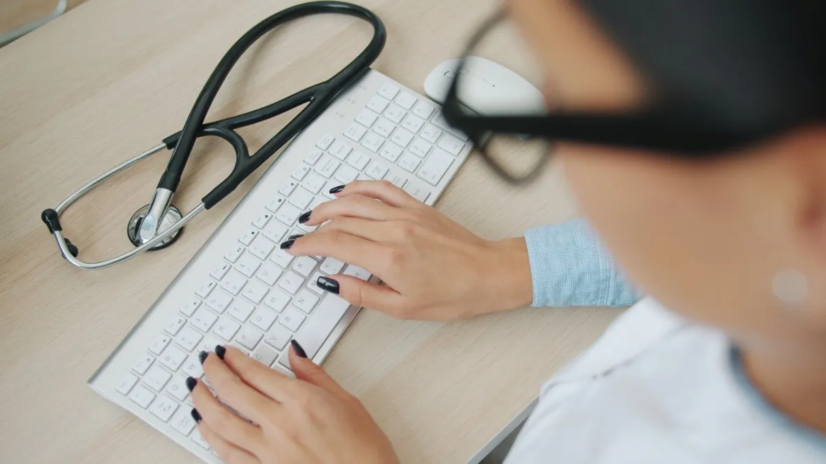 A clinician typing at her desk, with a stethoscope beside the keyboard.
